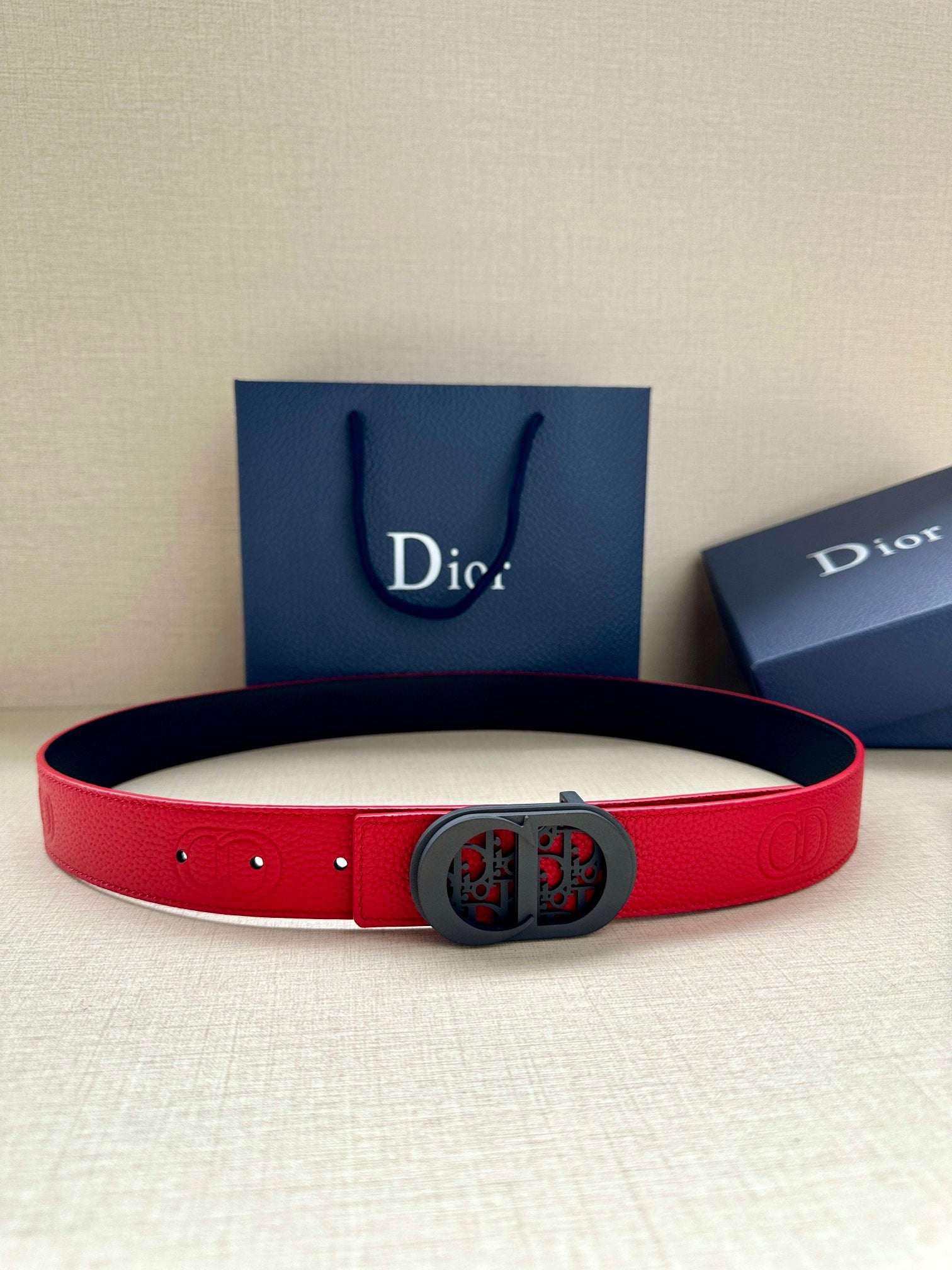 Dior belt in red leather with dark oval logo buckle and punched holes.