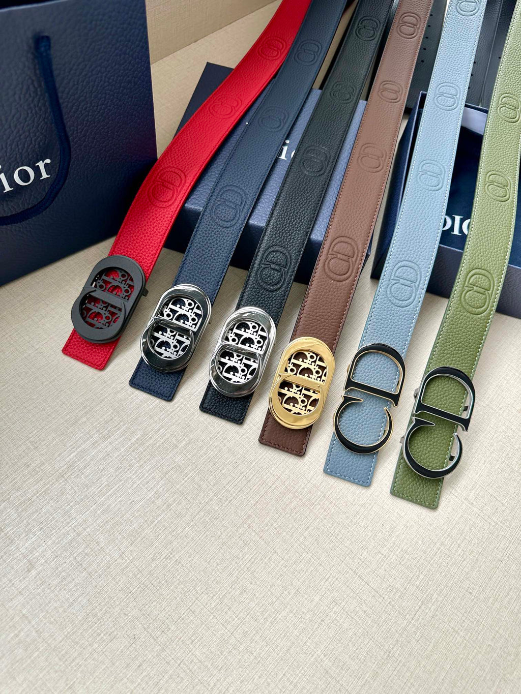 Assorted leather Dior belts with oval logo buckles in red, blue, beige, and green tones.