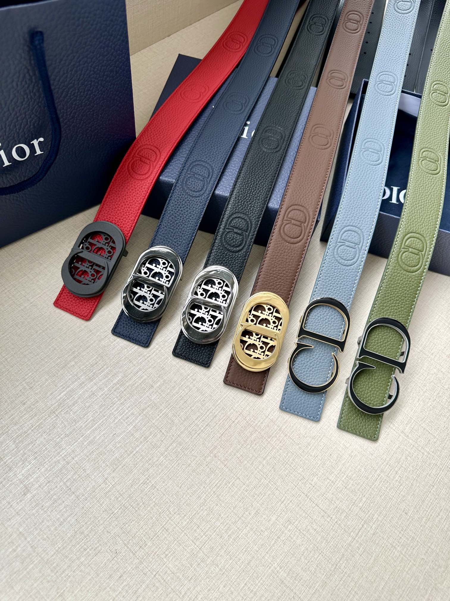Assorted leather Dior belts with oval logo buckles in red, blue, beige, and green tones.