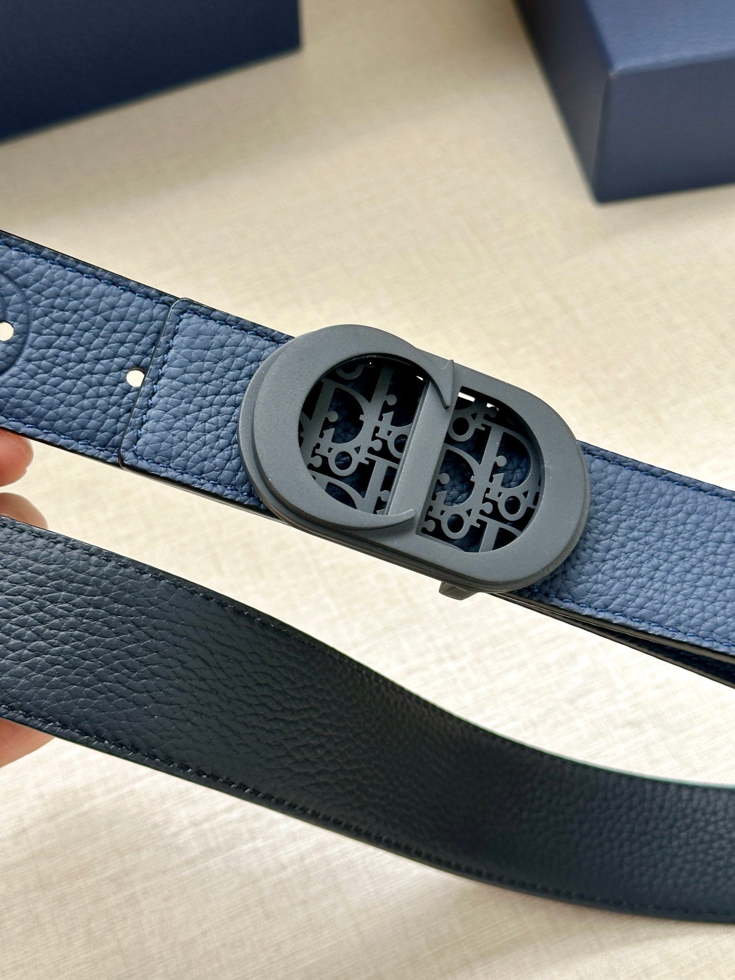 Dior belt buckle close-up with engraved oval emblem on blue leather