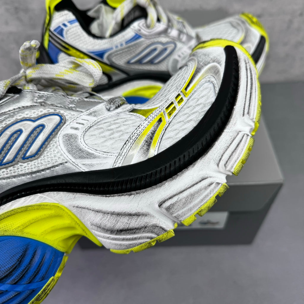 Close-up of silver sneaker upper with blue emblem and neon yellow trim