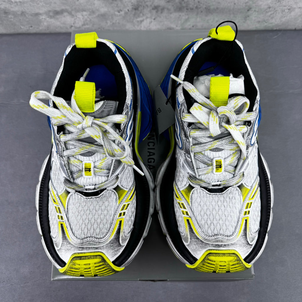 Front view of silver sneakers with neon yellow straps and blue emblem details