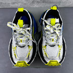 Front view of silver sneakers with neon yellow straps and blue emblem details