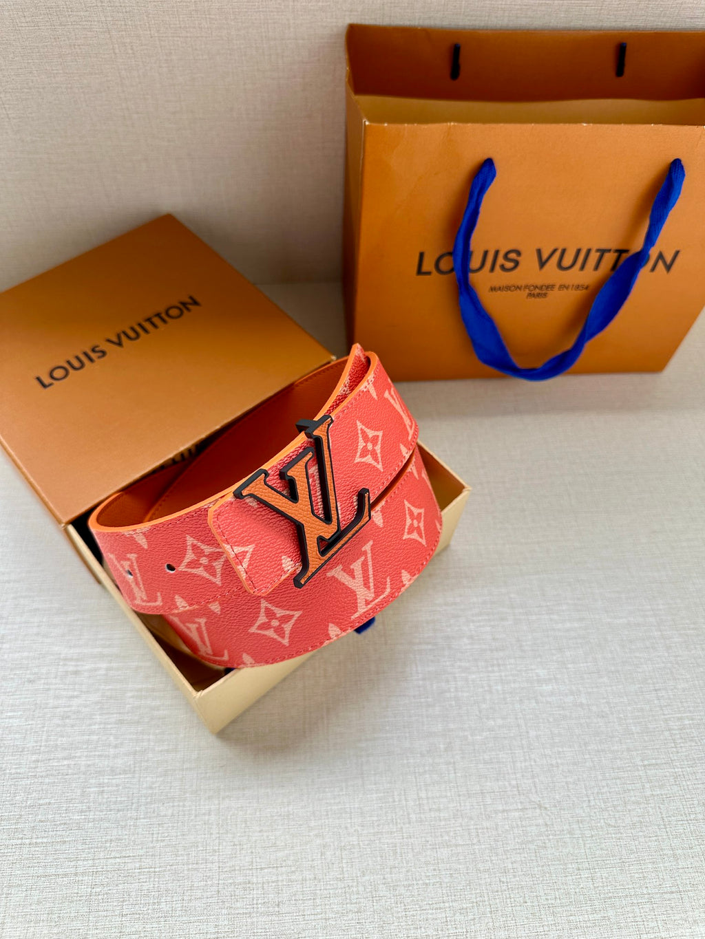 Louis Vuitton belt with red monogram strap and metal LV buckle, folded and angled