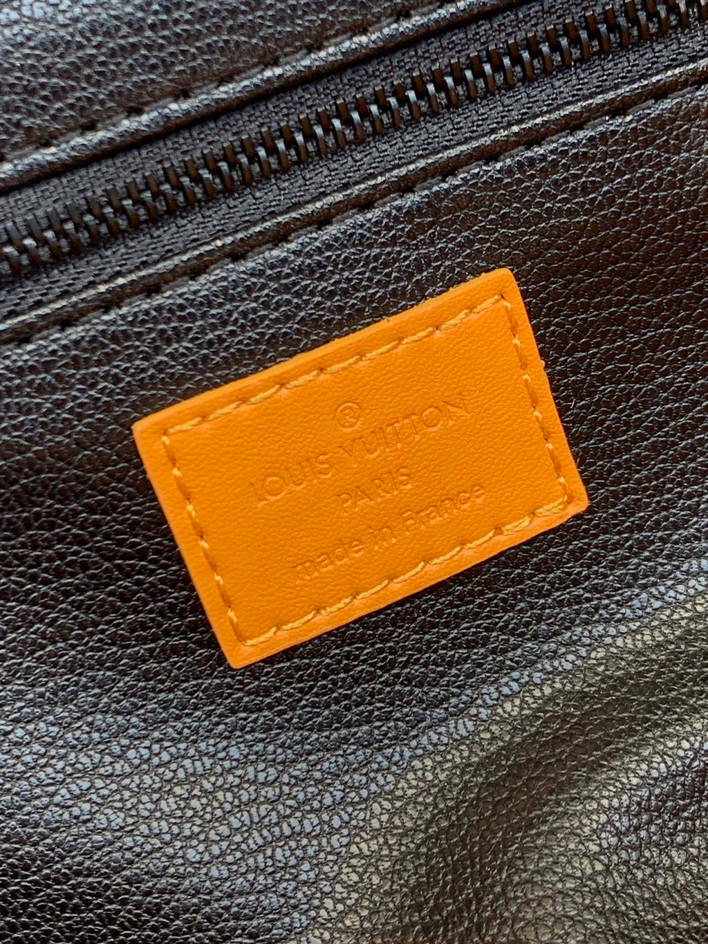 Tan label patch on dark leather bag exterior with embossed text