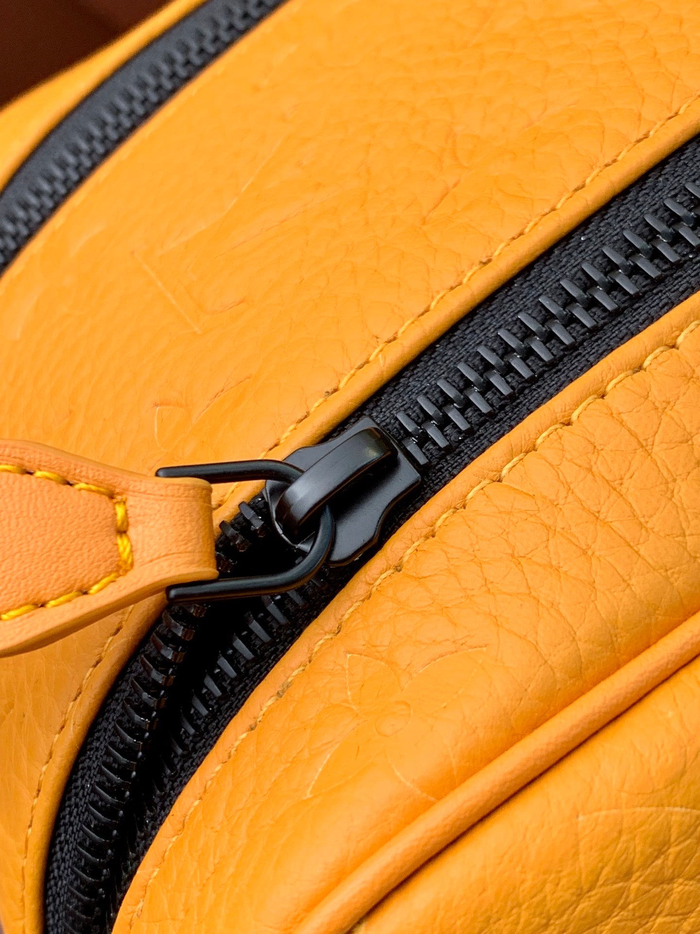 Mustard-yellow leather bag edge with black zipper track and metal ring