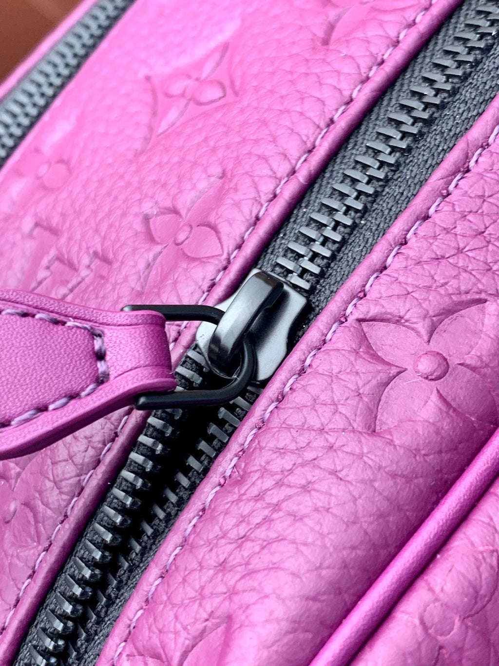 Purple embossed crossbody bag close-up with black zipper pull and stitched trim