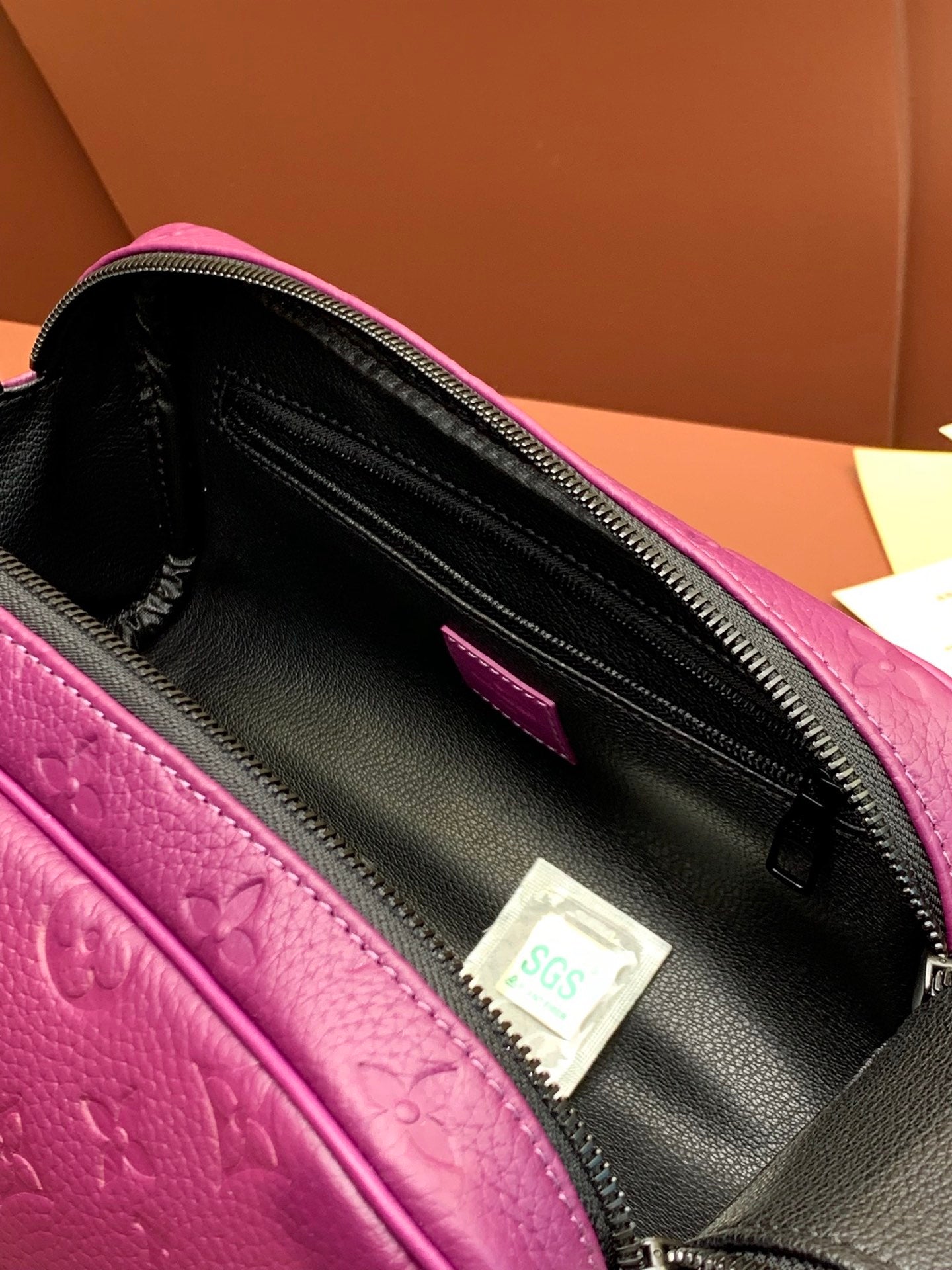 Purple embossed crossbody bag interior with black zipper track and hanging tag