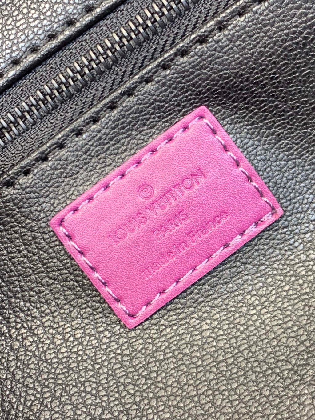 Pink leather label patch on dark textured bag material with metal zipper teeth