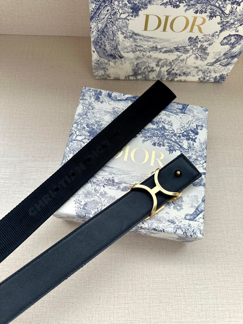 Designer belt with dark navy strap and gold CD buckle, eyelet side.