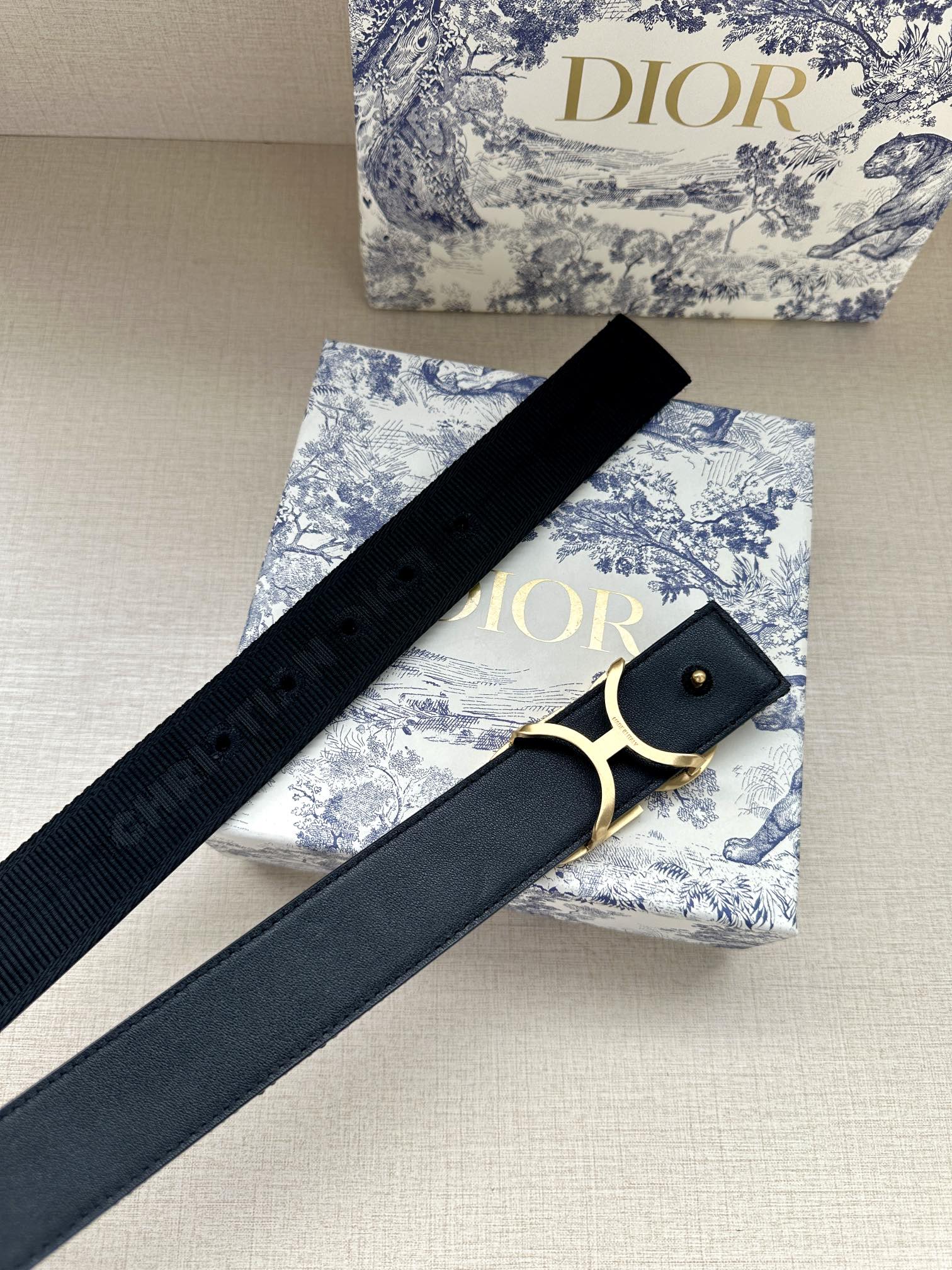 Designer belt with dark navy strap and gold CD buckle, eyelet side.