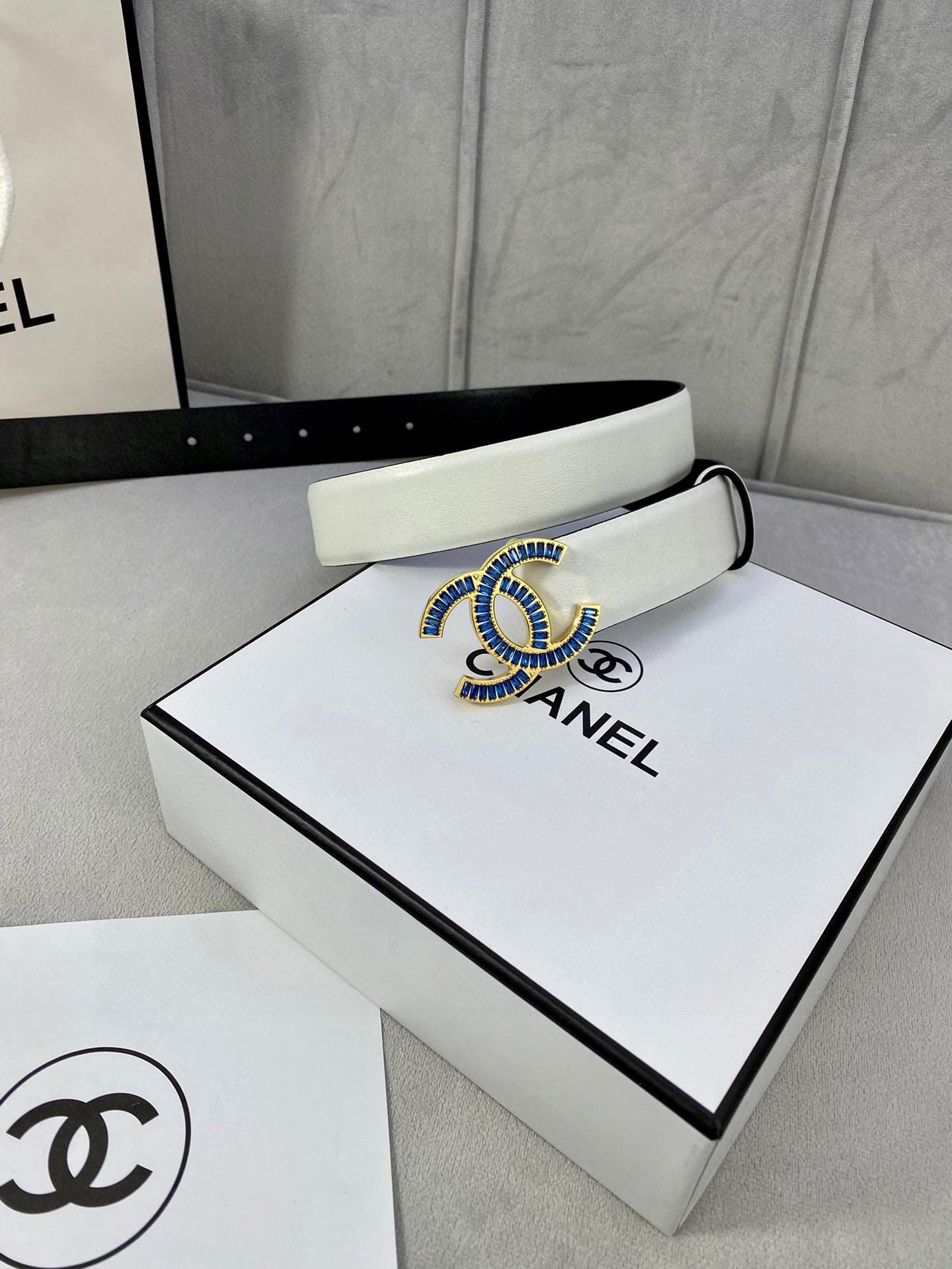 White leather belt with blue CC buckle on presentation box lid.