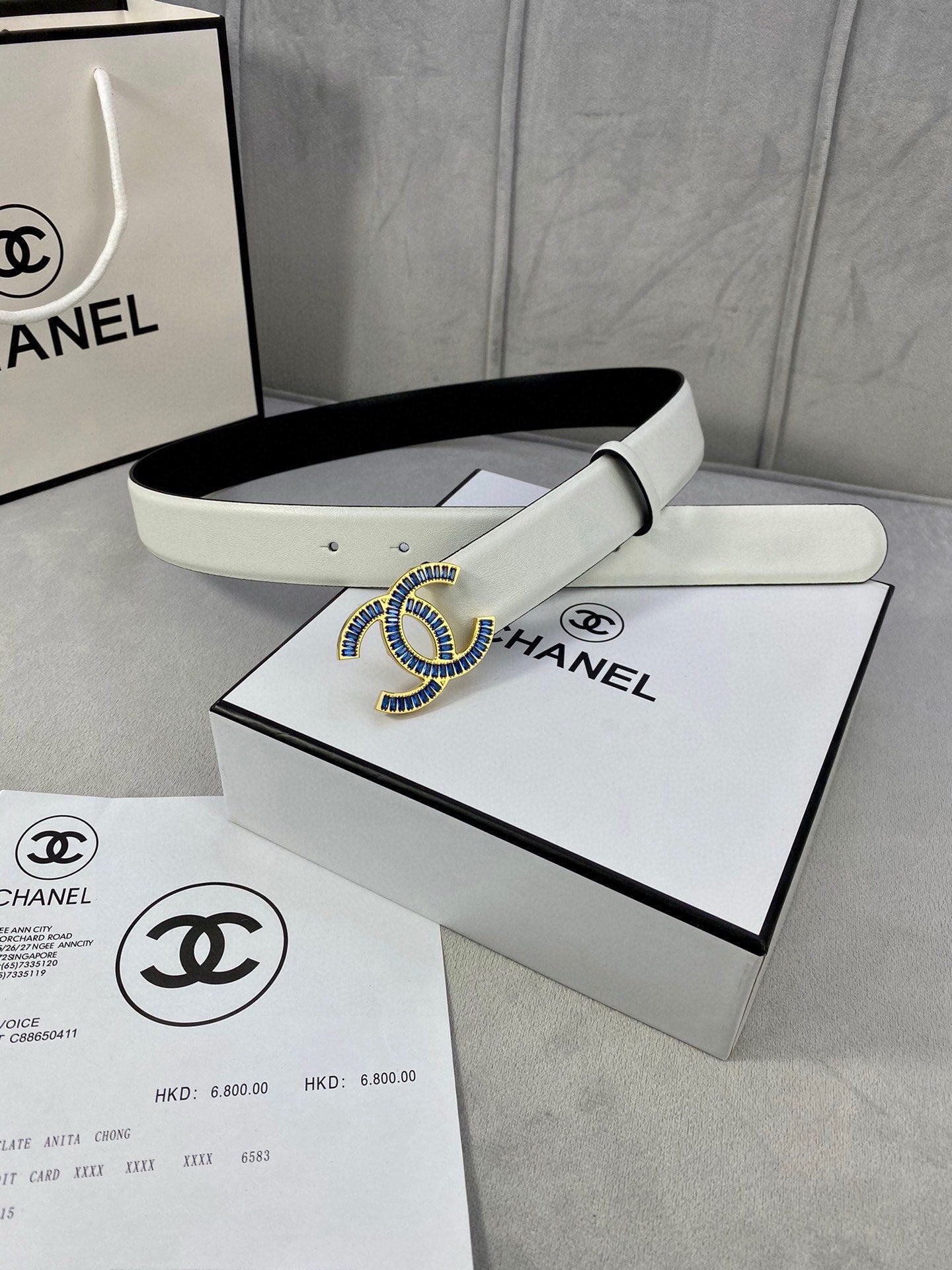 White leather belt with blue CC buckle on box, strap folded neatly.