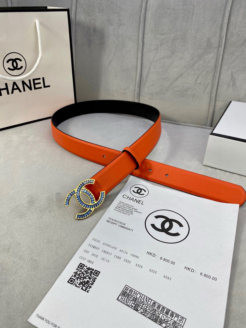 Belt: orange leather strap with blue-and-white CC logo buckle and punched holes.