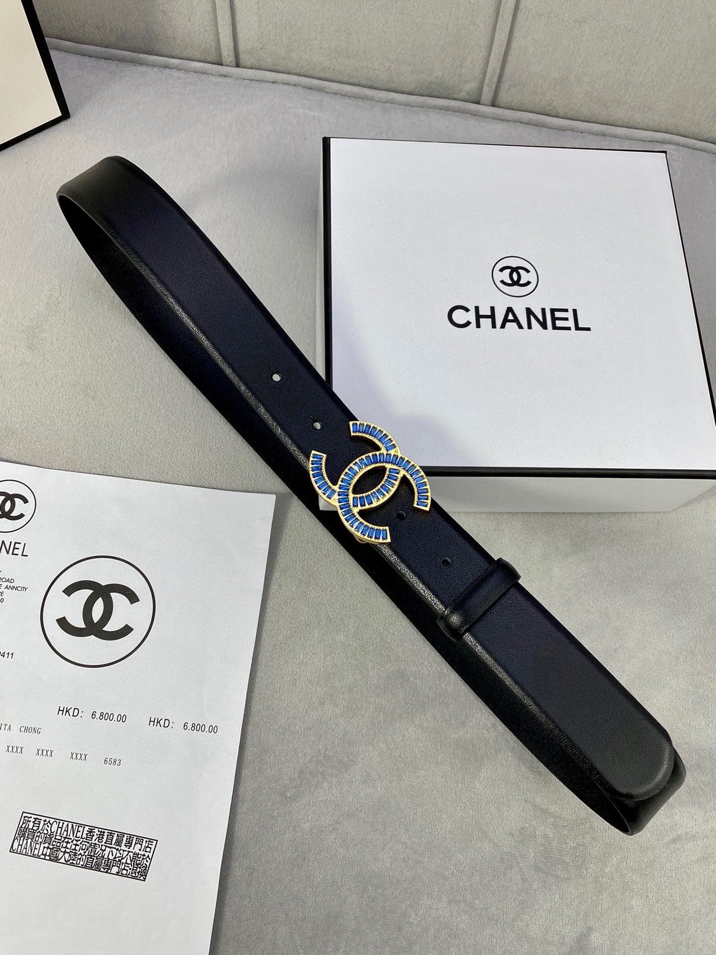 Black Chanel belt with blue jeweled CC buckle, laid across shopping bags