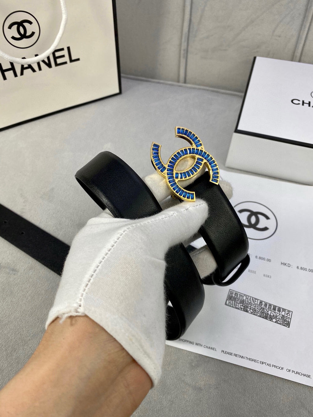 Black Chanel belt with blue jeweled CC buckle held in hand