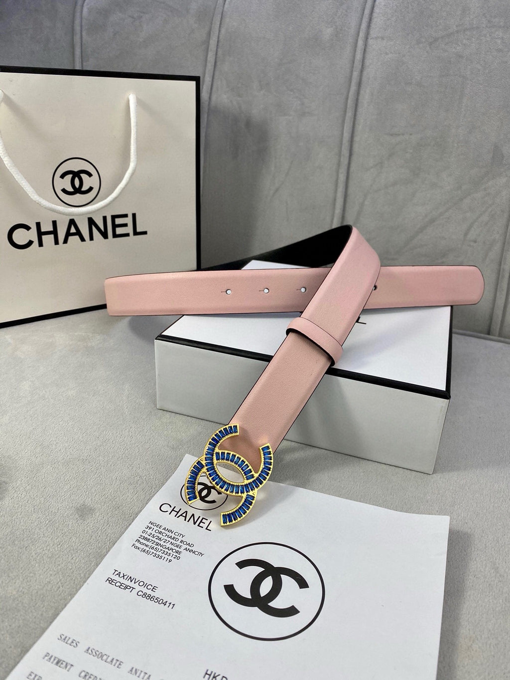 Chanel belt in pink leather with blue and gold CC-style buckle across box lid.