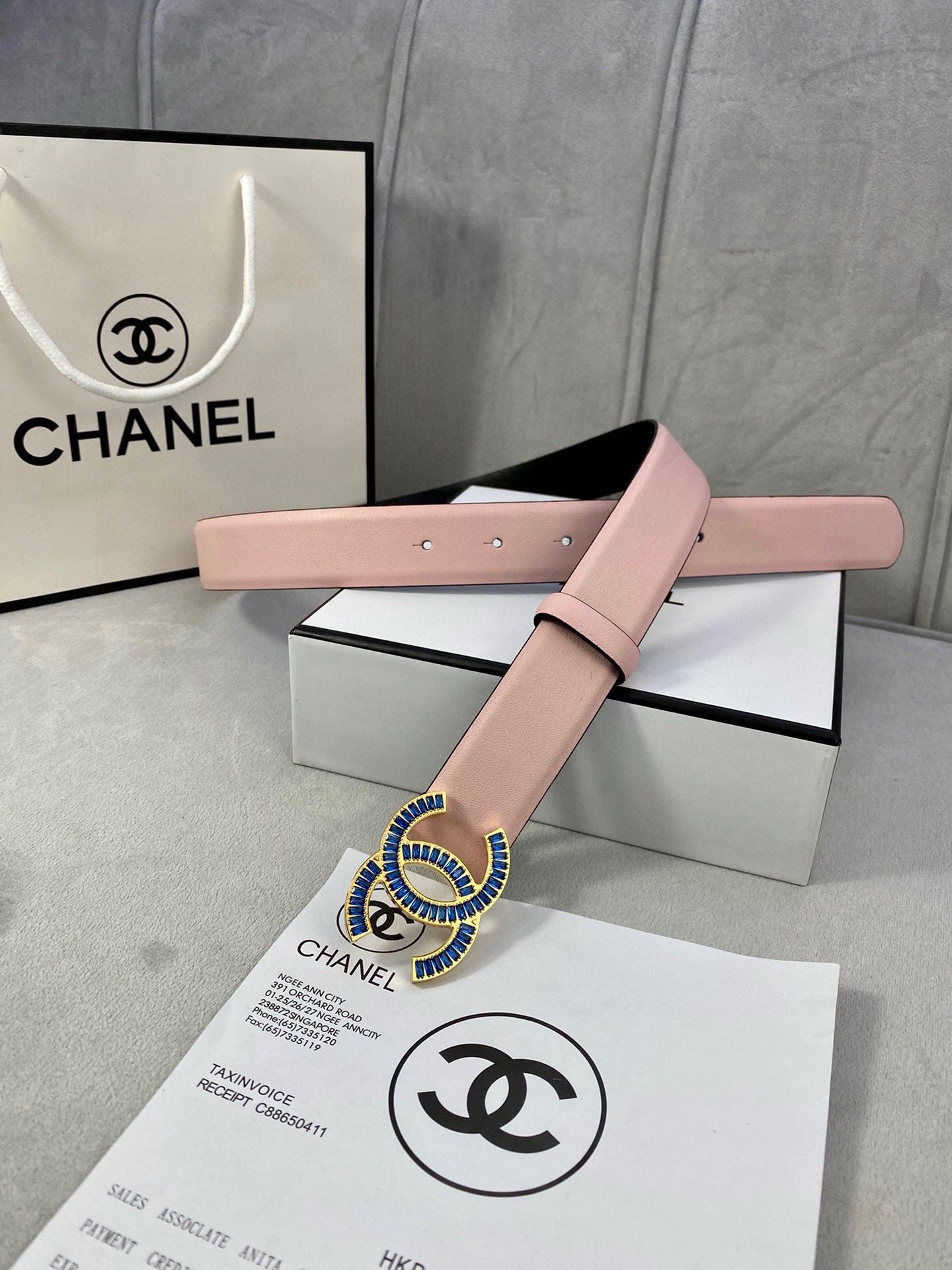 Chanel belt in pink leather with blue and gold CC-style buckle across box lid.