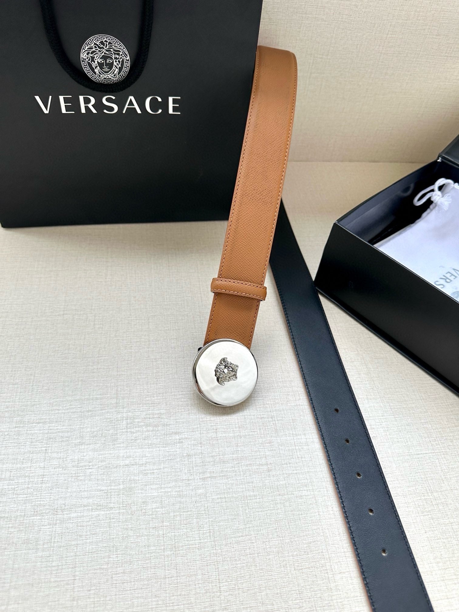 Tan leather belt with silver-toned round logo buckle and long strap end