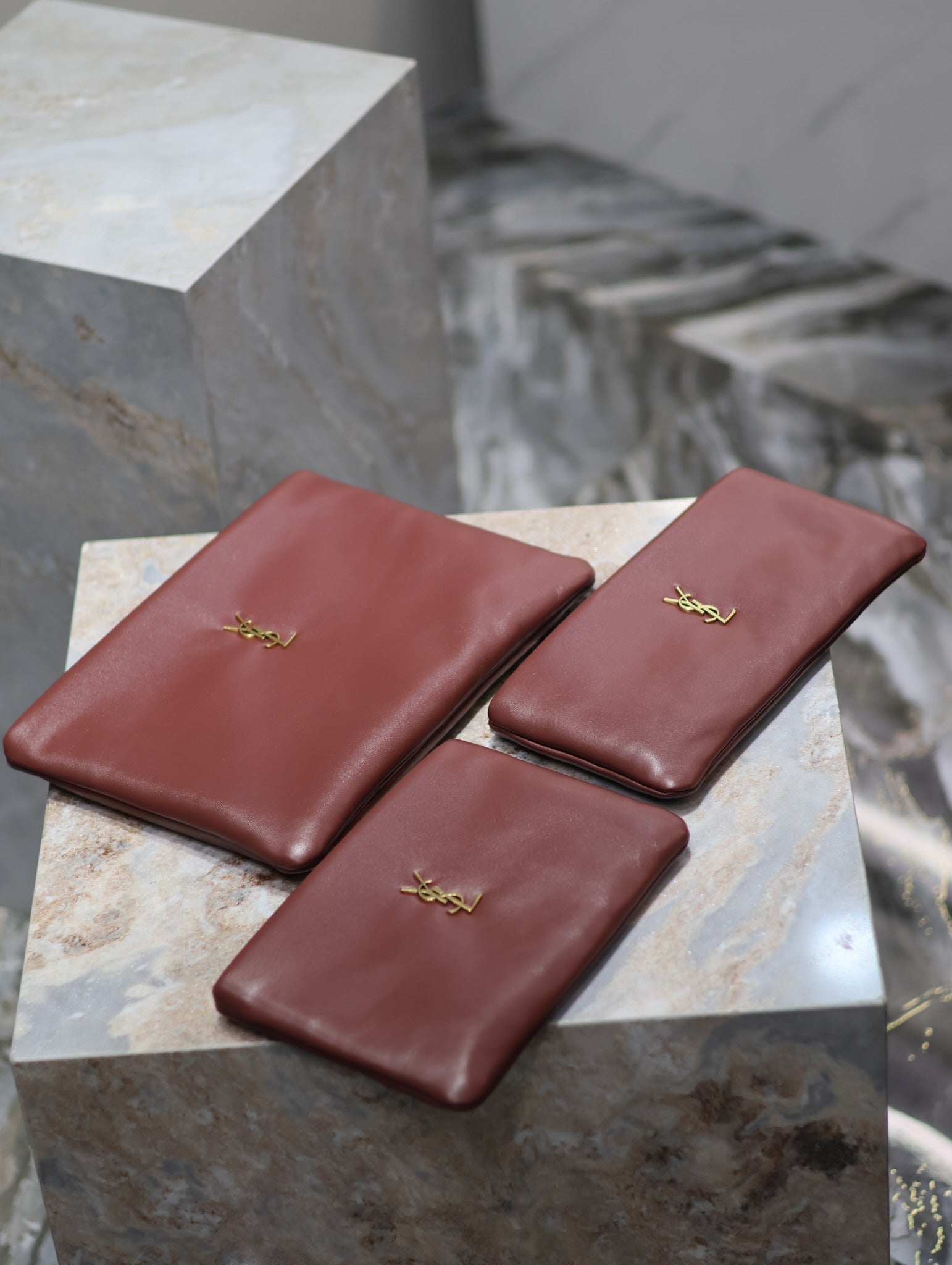 Burgundy leather small bags with gold YSL logo, three clutches on display