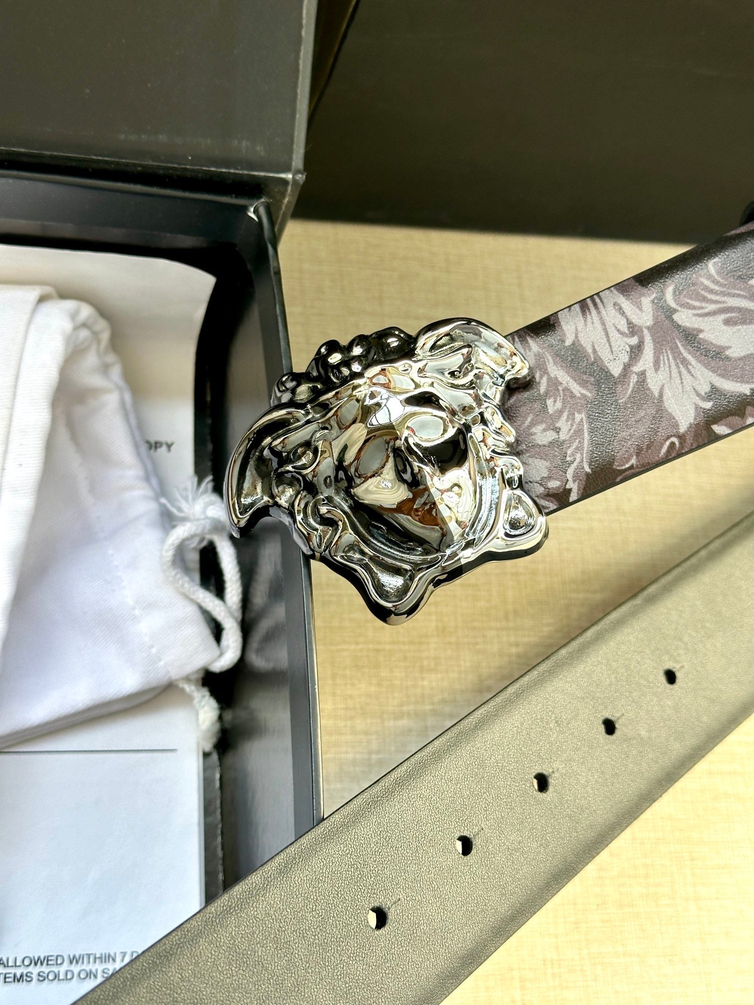 Floral belt detail with silver Medusa buckle and punched holes