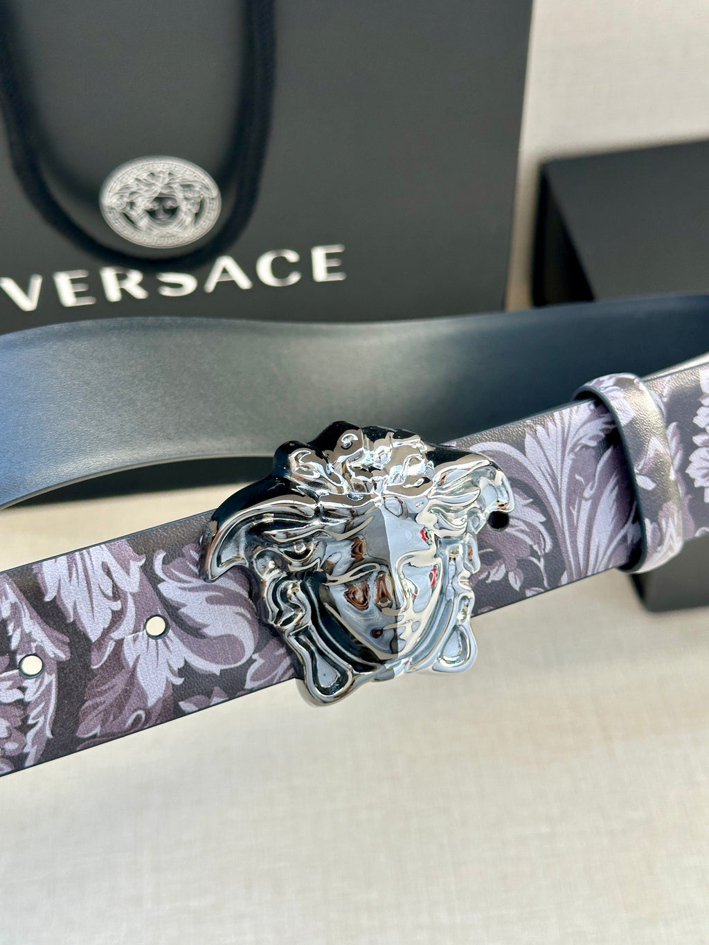 Floral leather belt close-up with silver Medusa buckle and dark strap