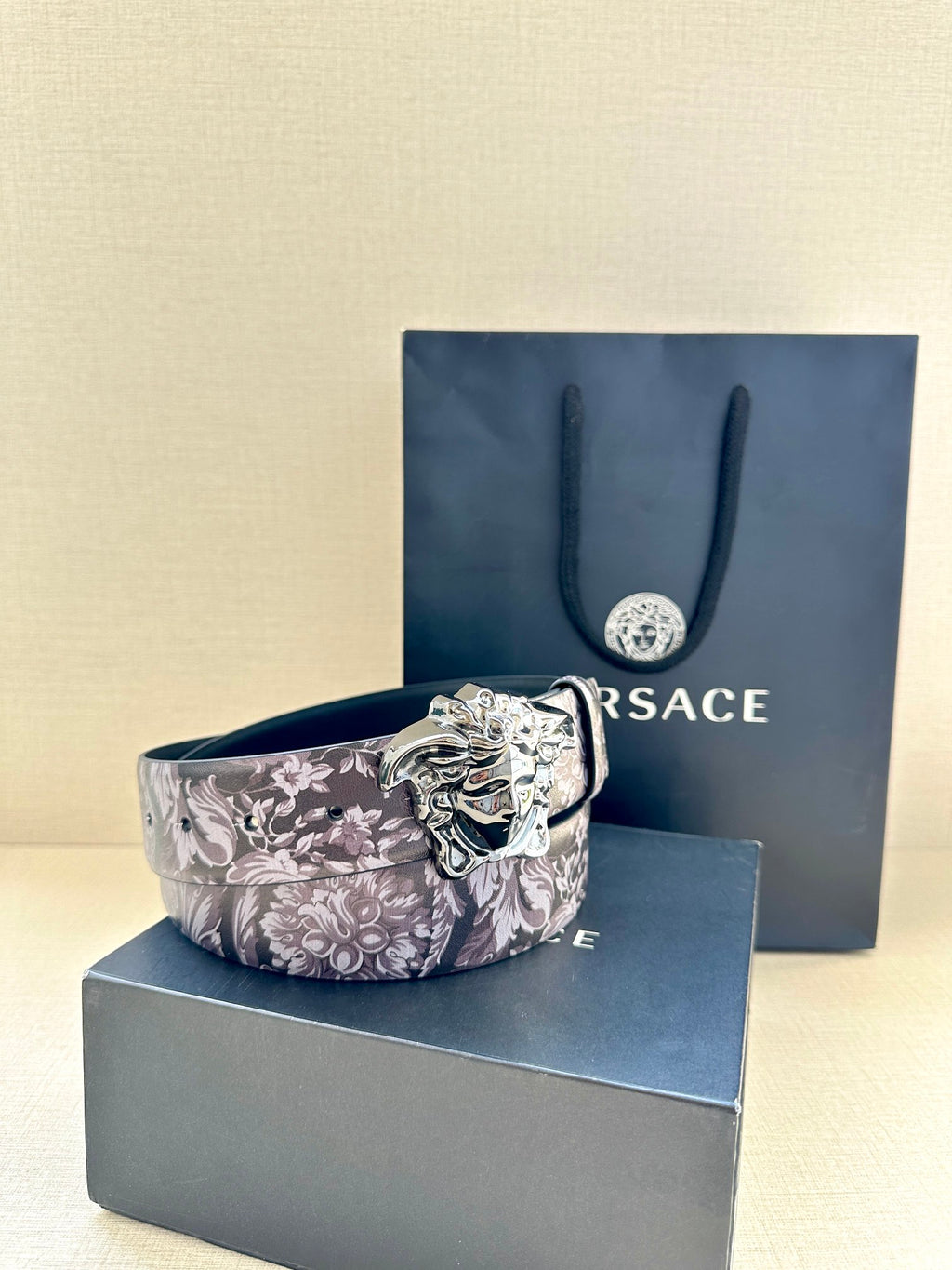 Floral leather belt with silver Medusa buckle, folded with blue packaging