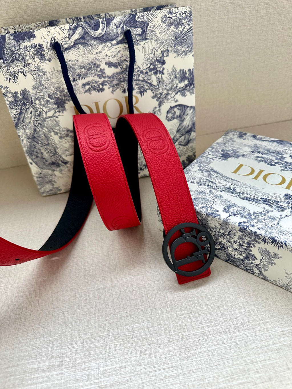 Red leather belt with oval logo buckle and textured strap, punched holes.
