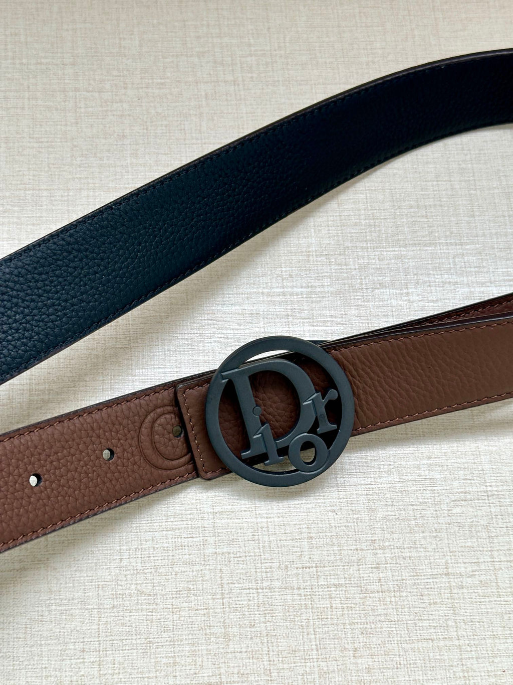 Dior belt close-up with textured dark blue strap and round logo buckle