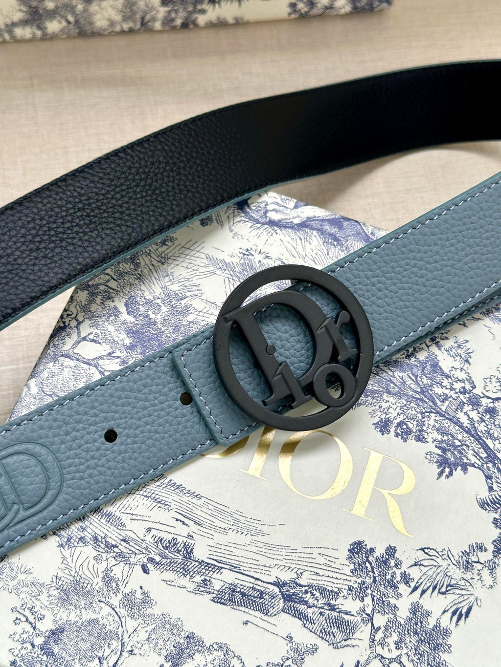 Dior belt detail: light blue textured strap with round dark CD buckle and hole end