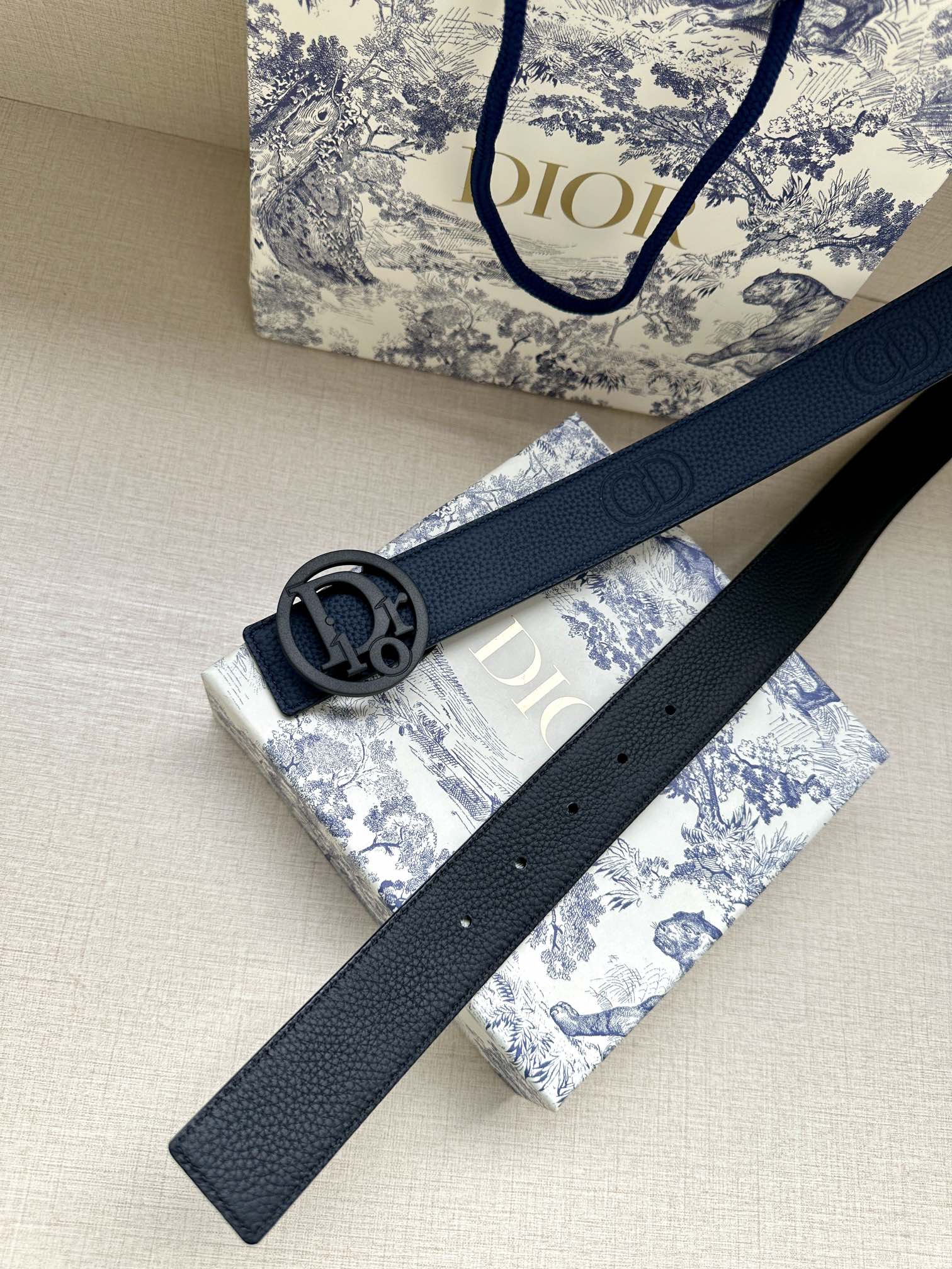 Blue leather belt with oval logo buckle and punched adjustment holes.