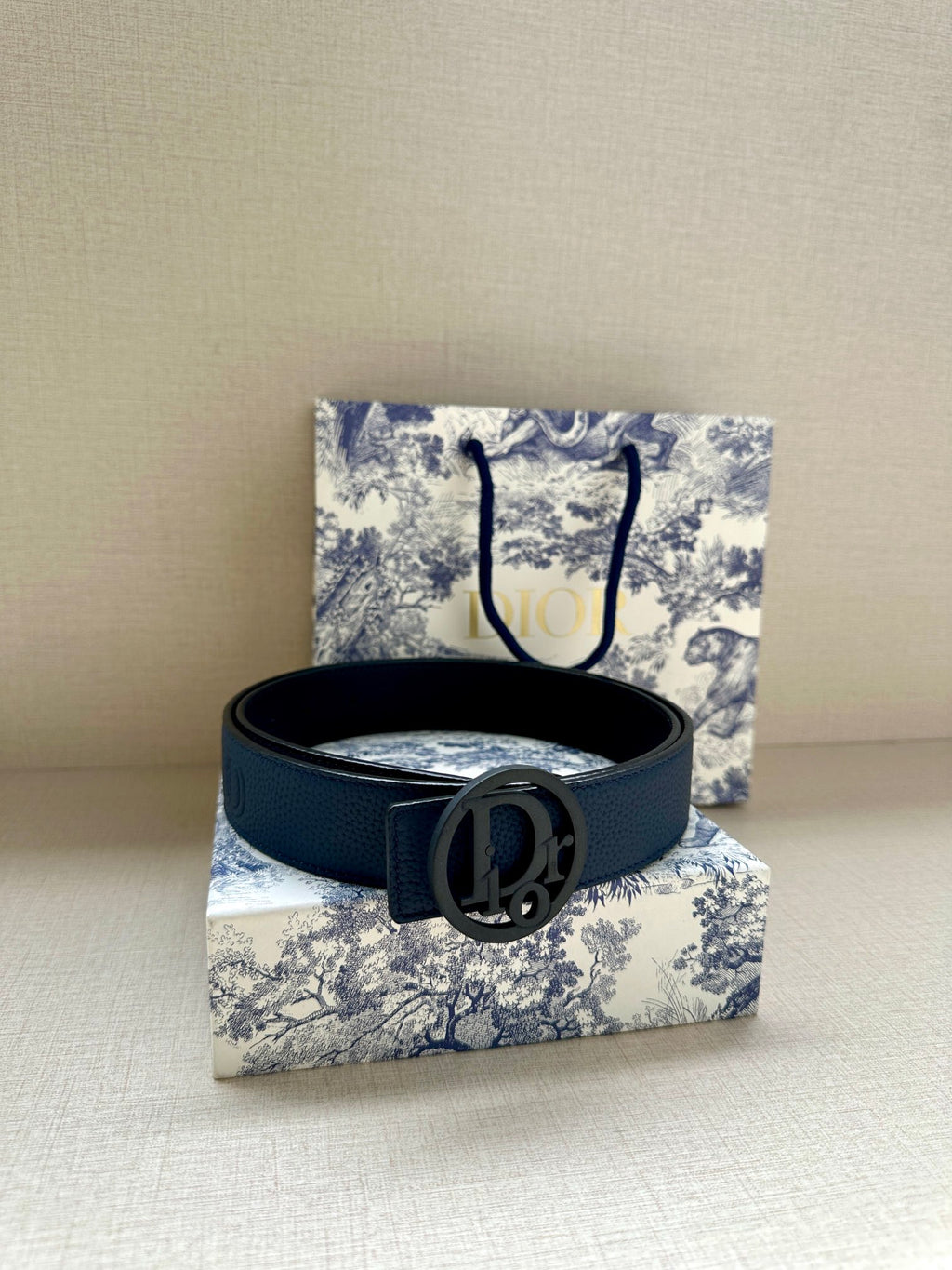Blue leather belt with oval logo buckle, resting on a flat surface.