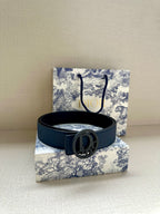 Blue leather belt with oval logo buckle, resting on a flat surface.