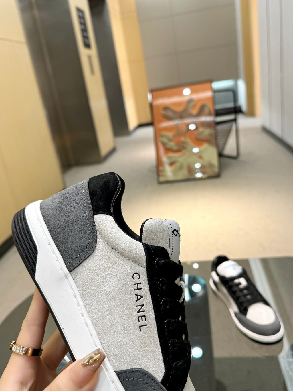 Chanel unisex sneaker side view, gray and white panels with black laces and logo tab