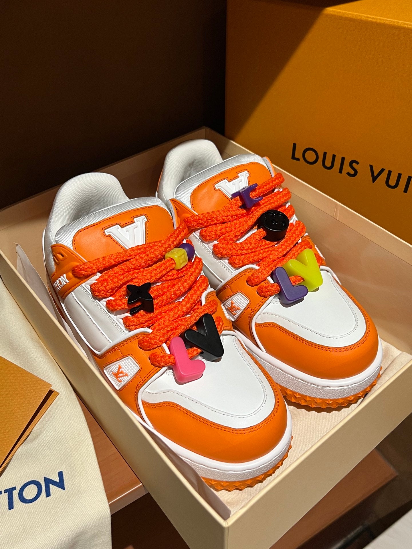 Pair of orange and white Louis Vuitton trainer sneakers with colorful lace decorations
