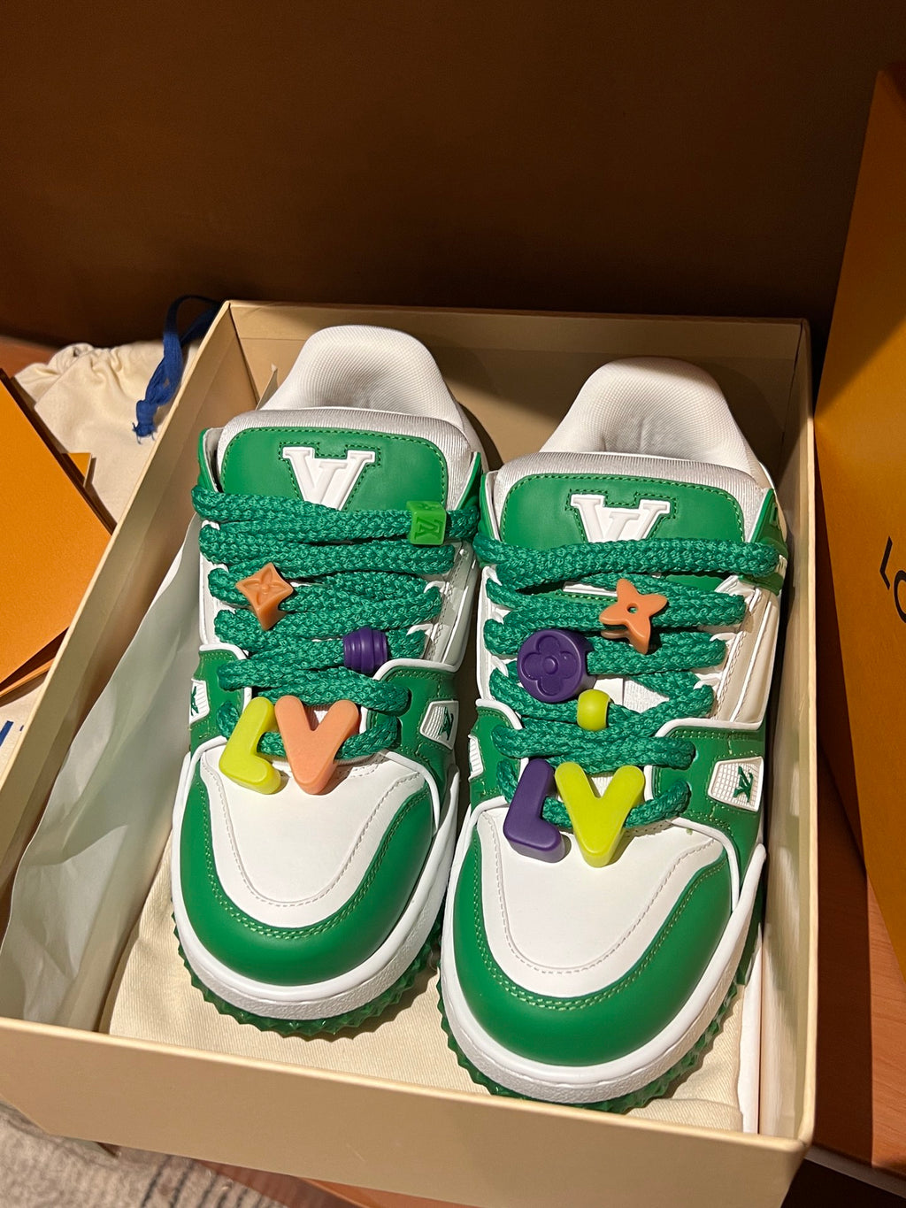 Green-and-white low-top sneakers with colorful lace charms in a shoe box