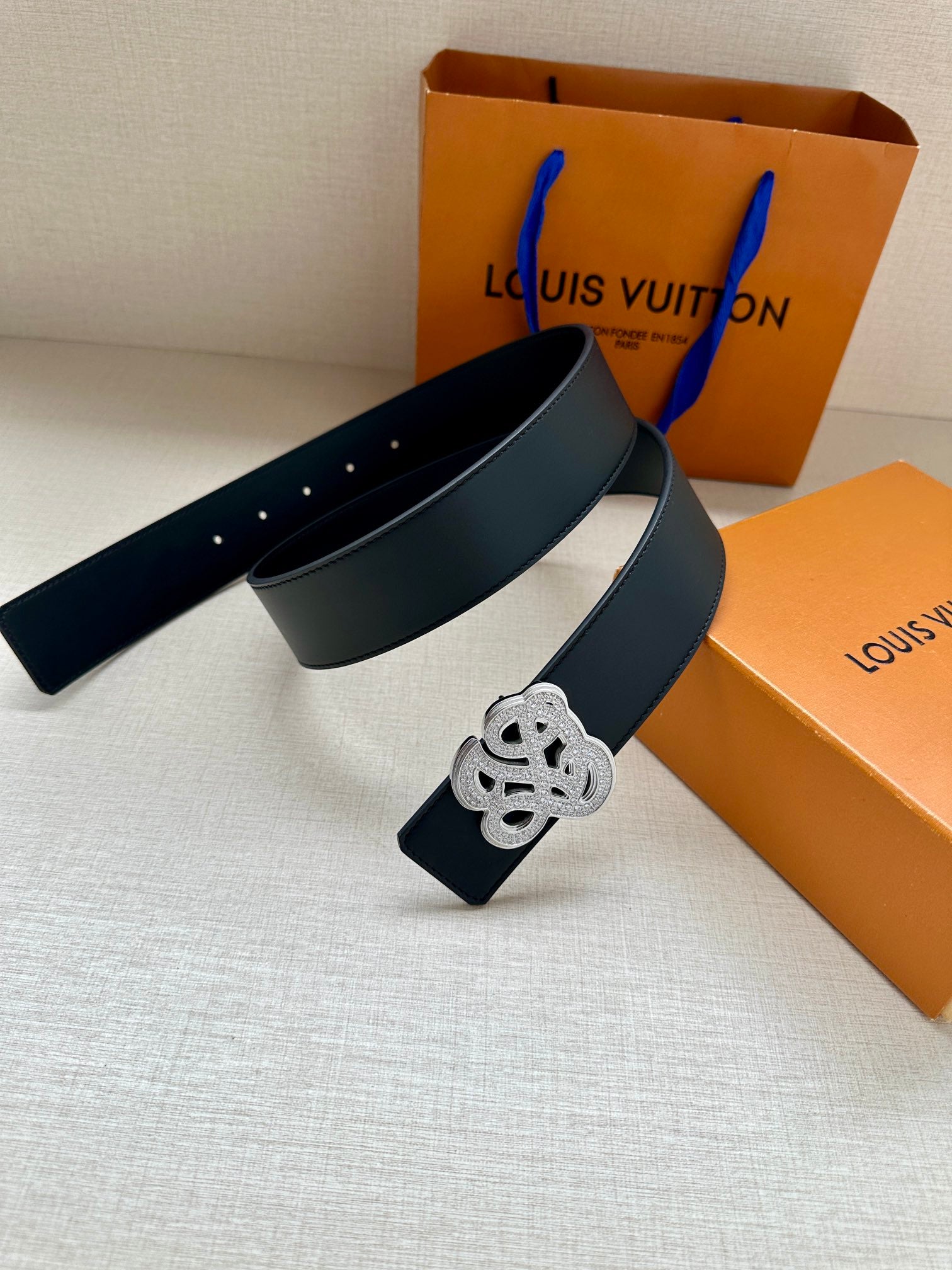 Dark blue leather belt with silver-tone monogram buckle and perforated end.