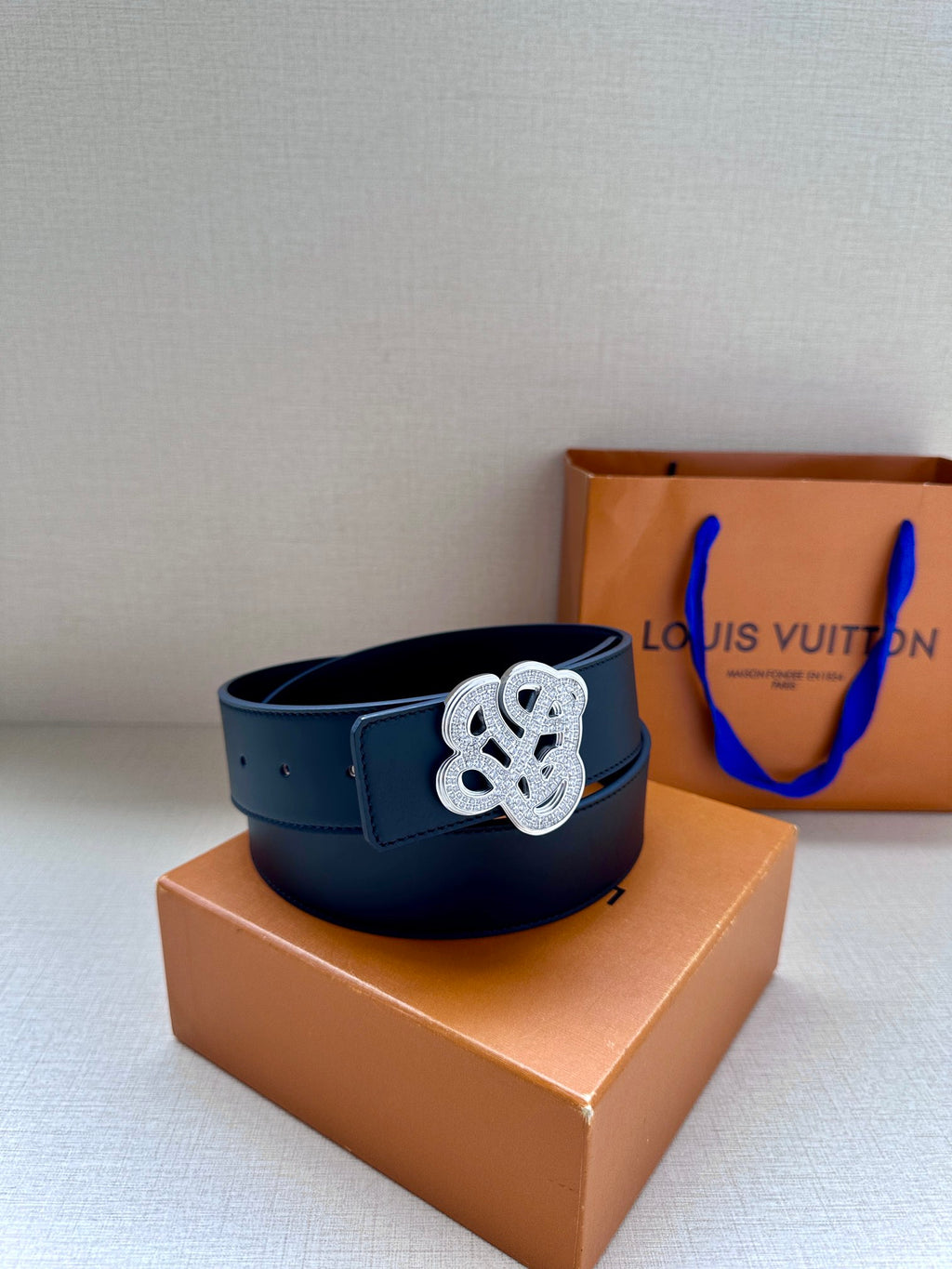 Dark blue leather belt with silver-tone monogram buckle resting on box.