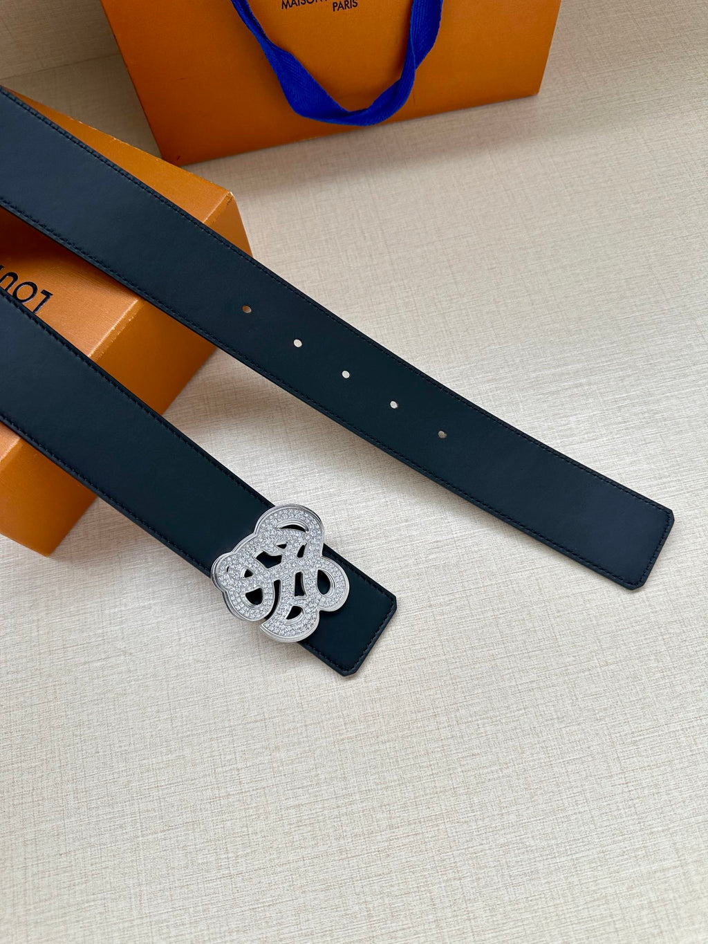 Dark blue leather belt strap with silver-tone monogram keeper, eyelets visible.