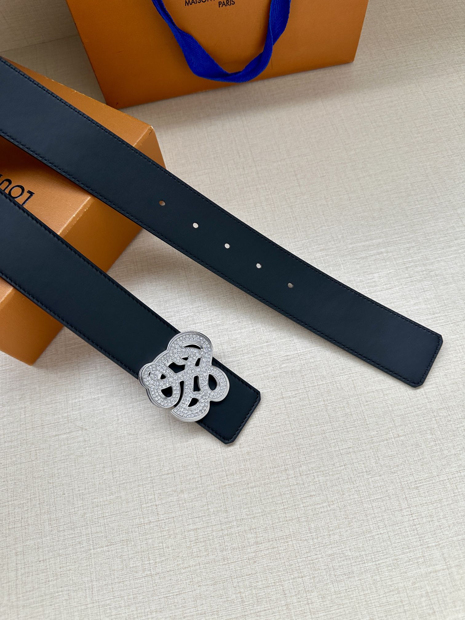 Dark blue leather belt strap with silver-tone monogram keeper, eyelets visible.