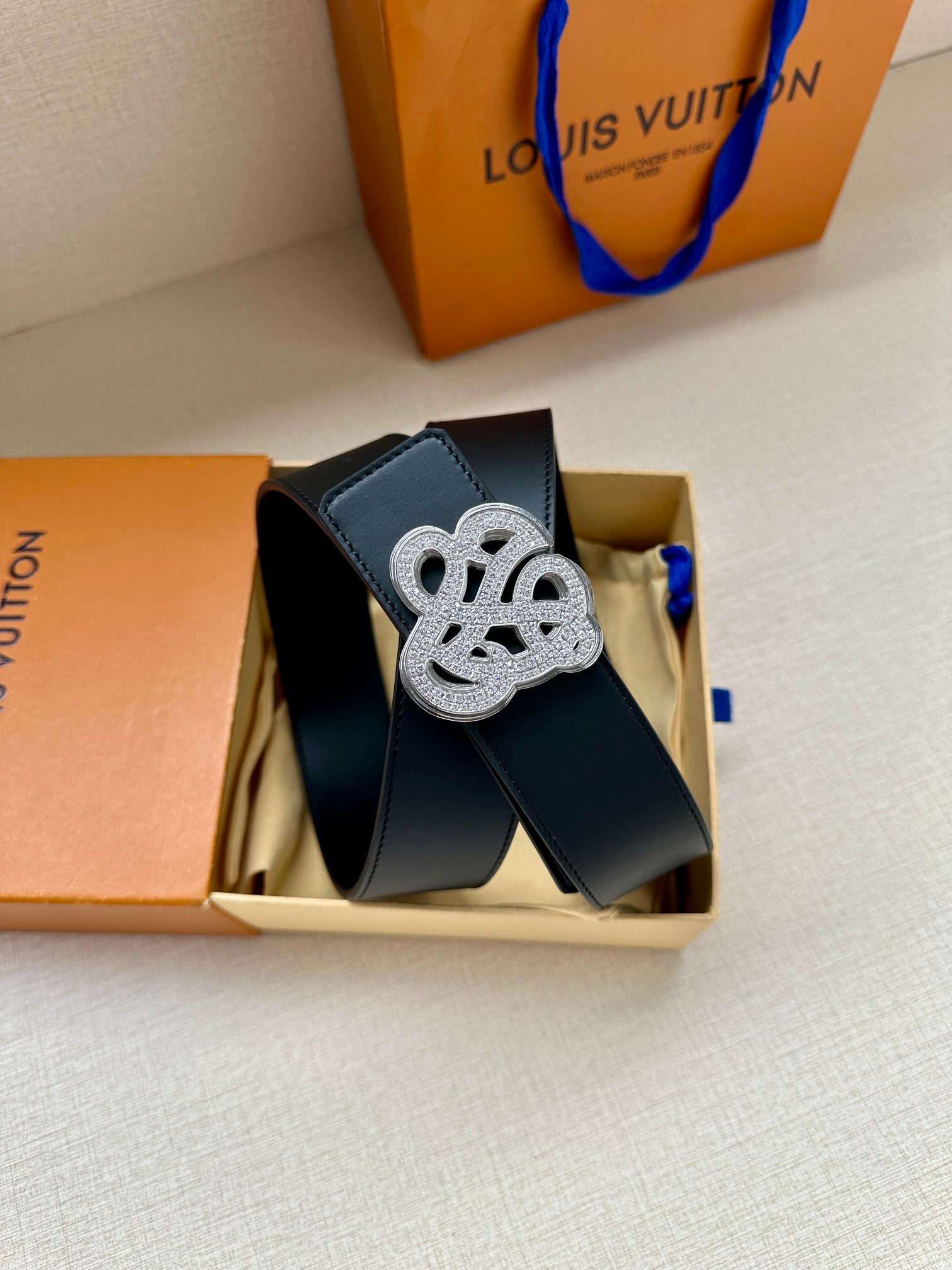 Dark blue leather belt with silver-tone monogram buckle, keeper strap shown.