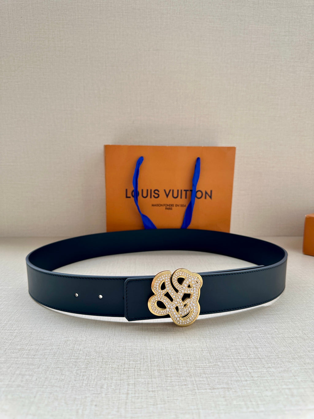 Dark blue leather belt with silver-tone monogram buckle, multiple eyelets.