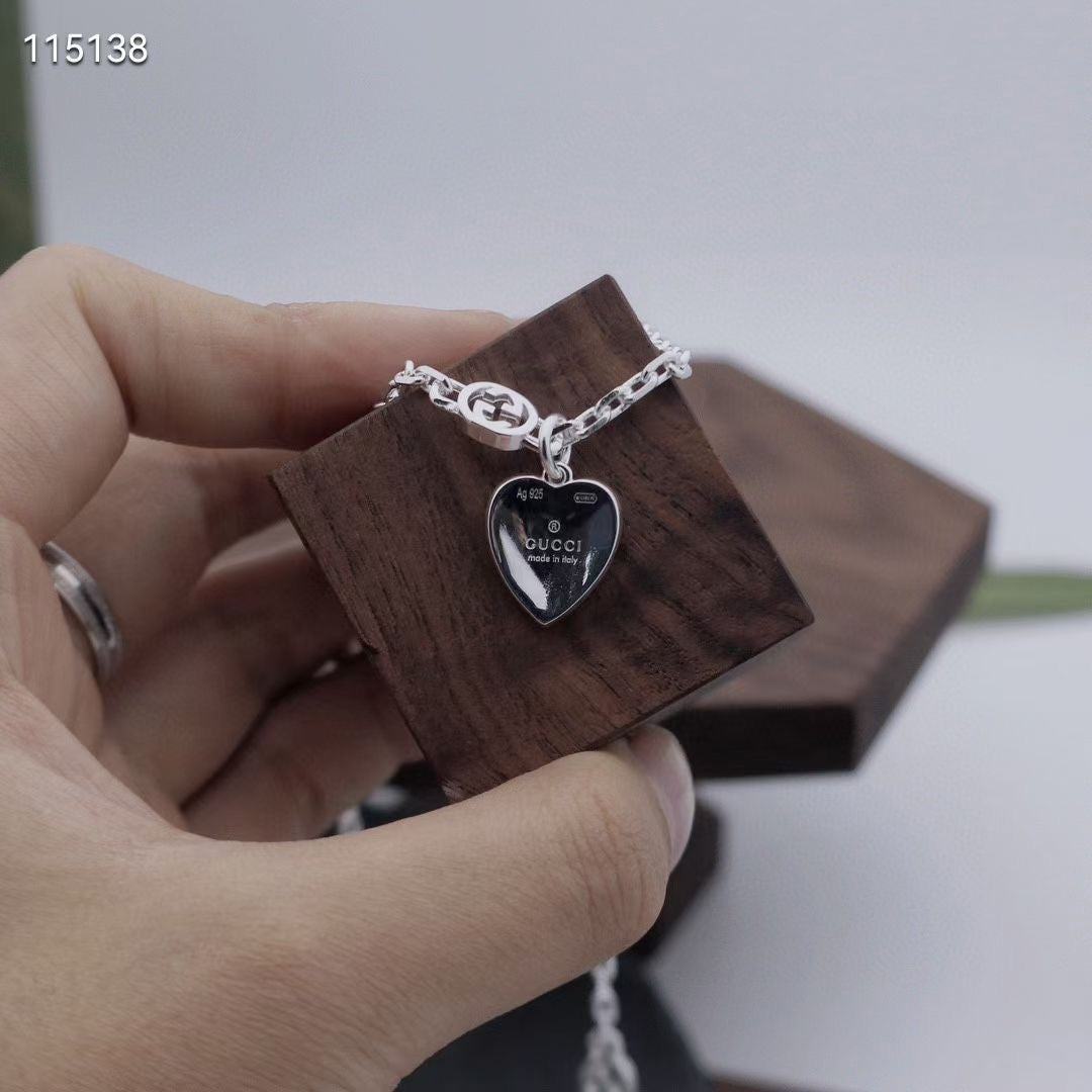 Gucci silver heart pendant necklace held in hand on a wooden display block