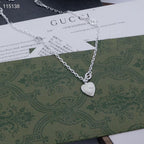 Gucci silver heart pendant necklace resting on a patterned green shopping bag
