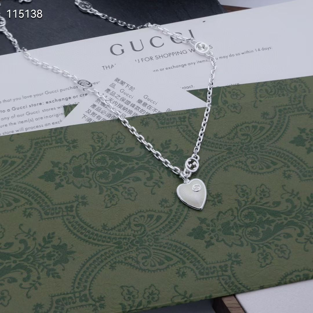 Gucci silver heart pendant necklace resting on a patterned green shopping bag