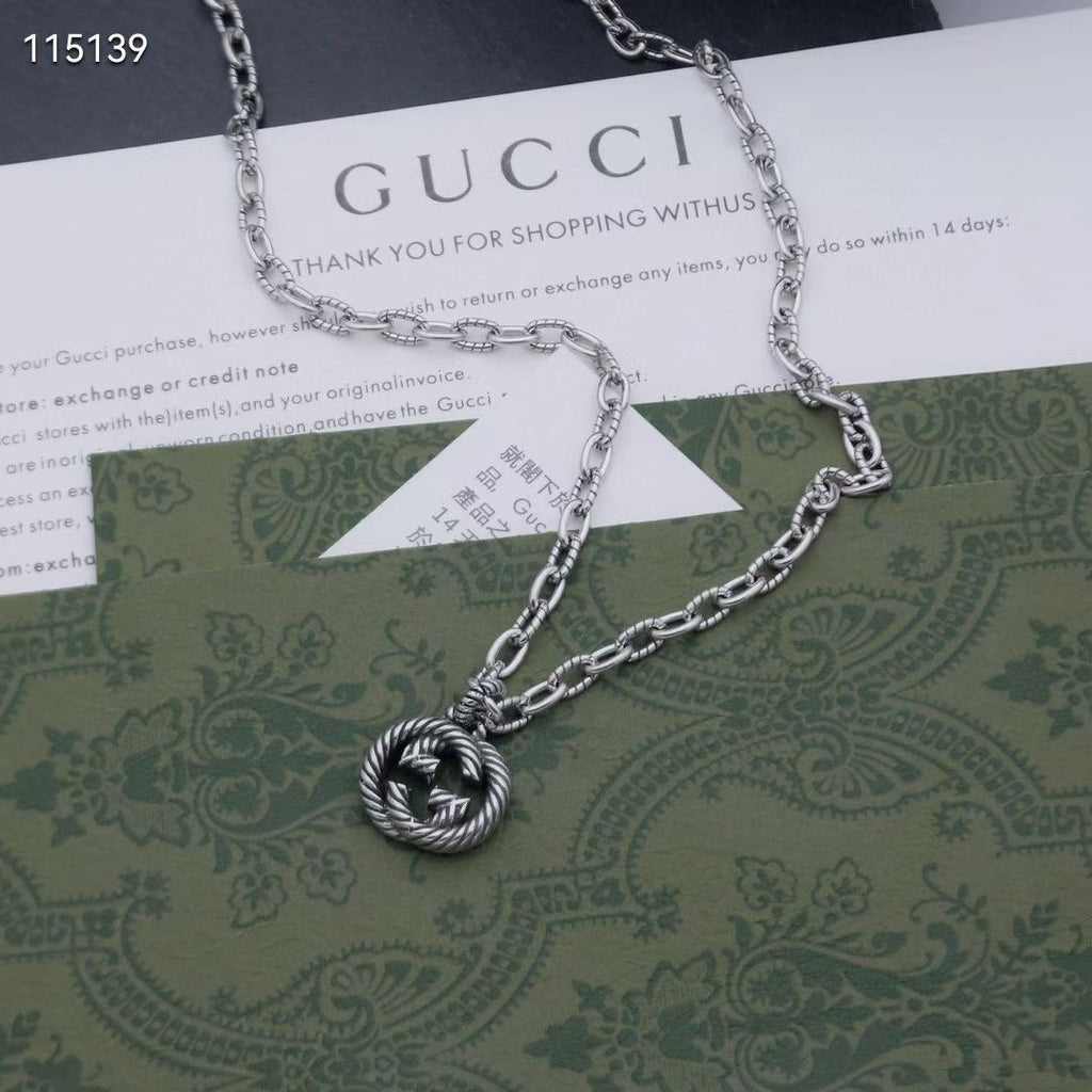Silver-tone chain necklace with round knot pendant, laid over a green card