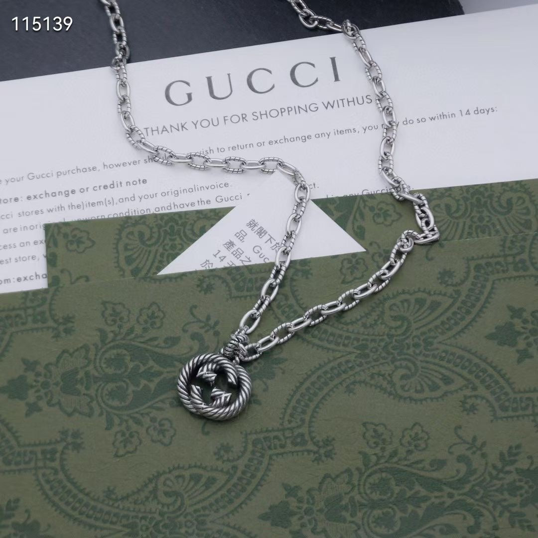 Silver-tone chain necklace with round knot pendant, laid over a green card