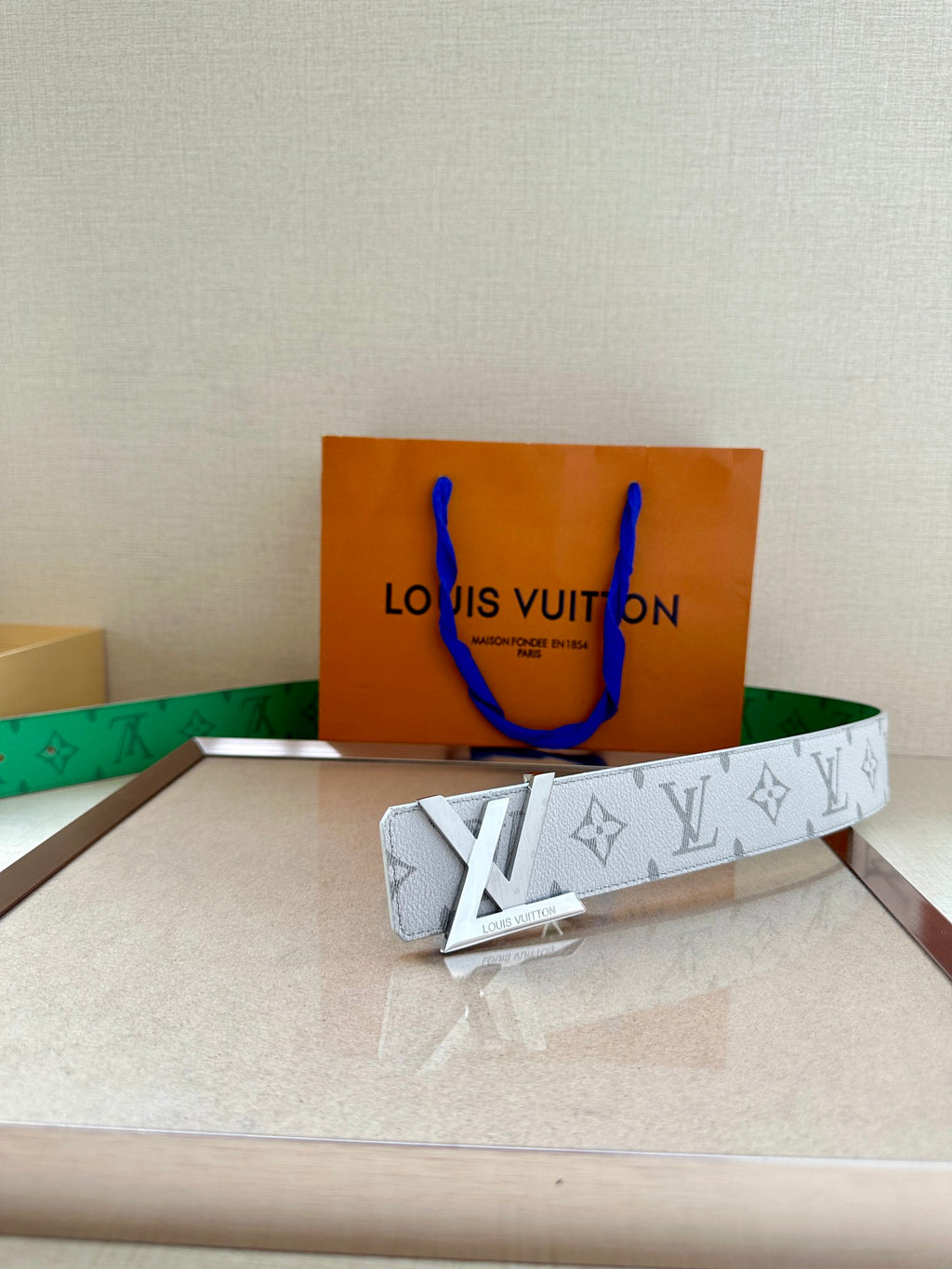 White monogram belt with green lining and gold buckle on box