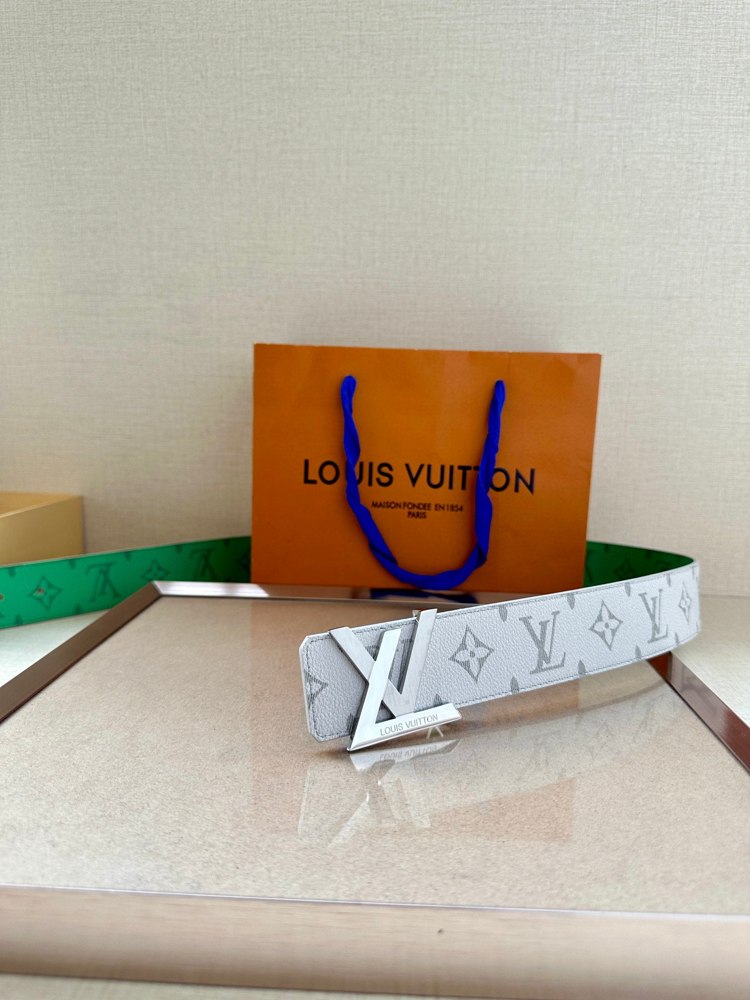 White monogram belt with green lining and gold buckle on box
