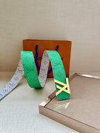 Green and gray monogram belt with gold buckle, laid across boxes
